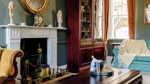 A room with a fireplace, a blue sofa, a wooden coffee table, and a cabinet with glass doors. - The Admirals House - Central Bath & Free Parking! (Bath)