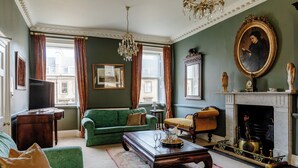 A traditional living room with a green sofa, a wooden coffee table, and a fireplace with a decorative mantel. - The Admirals House - Central Bath & Free Parking! (Bath)