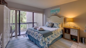 A bedroom with a bed, a nightstand, a lamp, a painting, and a view of the outdoors.