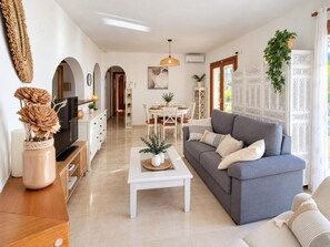 A modern living room with a grey sofa, white coffee table, and a TV on a wooden stand. - Casa de Sueños - Benitachell, Costa Blanca (Benitachell)