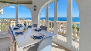 Comedor con mesa preparada para cuatro, ventanas arqueadas amplias y vistas al mar.