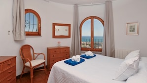 Una habitación de hotel con una cama, una silla, un aparador y dos ventanas con cortinas.