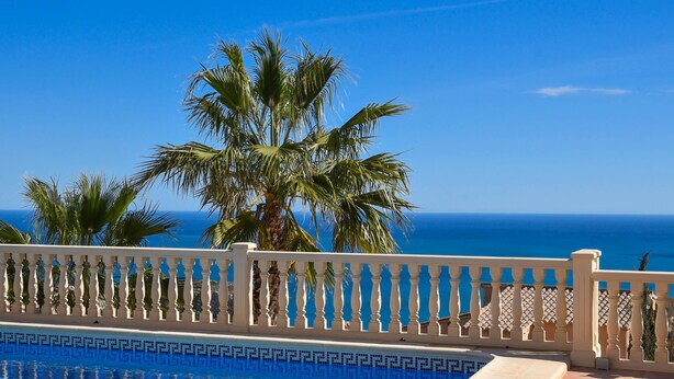 Una piscina con barandilla blanca, palmeras y vista al océano.