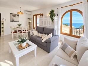 A modern living room with a gray sofa, a white coffee table, and a view of the sea through large windows. - Casa de Sueños - Benitachell, Costa Blanca (Benitachell)