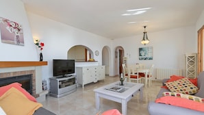 Una sala de estar moderna con chimenea, televisor, mobiliario blanco y un comedor.