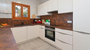 Una cocina moderna con armarios blancos, encimera de madera, horno empotrado y ventana con vistas al exterior.
