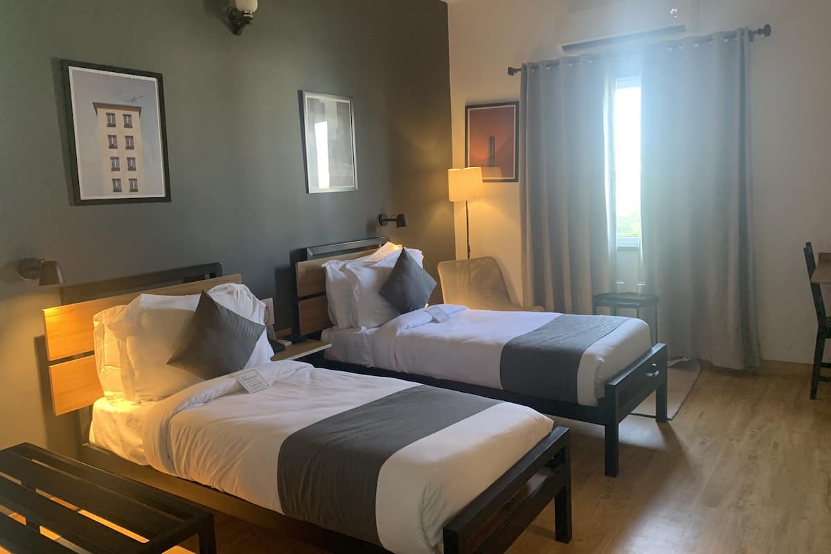 Habitación de hotel con dos camas, un escritorio, una silla y una ventana con cortinas.