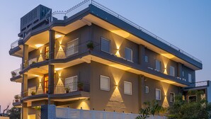 Un immeuble résidentiel à plusieurs étages, doté de balcons, d’un éclairage extérieur et d’une clôture blanche.