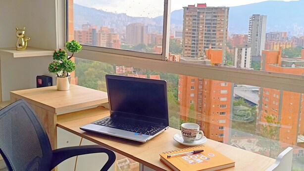 Ein moderner Arbeitsplatz mit einem Laptop, einer Kaffeetasse und einem Buch auf dem Schreibtisch, mit Blick auf eine Stadtlandschaft.