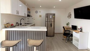 Eine moderne Küche mit integrierter Kochinsel, Barhocker, einem Kühlschrank, einer Mikrowelle und einem Flachbildfernseher.