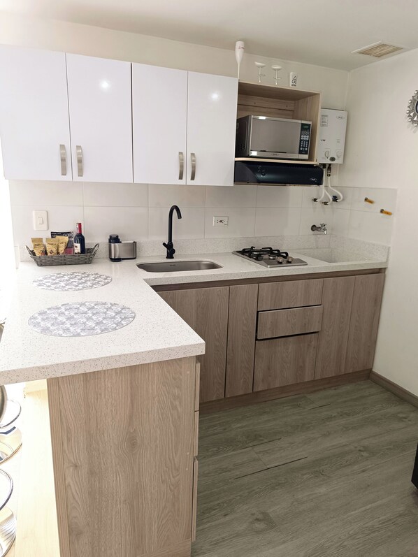 Una cocina con armarios blancos, un microondas, un fregadero y una estufa a gas.