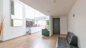 Eine großzügige Lobby mit modernem Design, ausgestattet mit einer Rezeption, einer Sitzecke und einer Tür zu einem weiteren Raum.