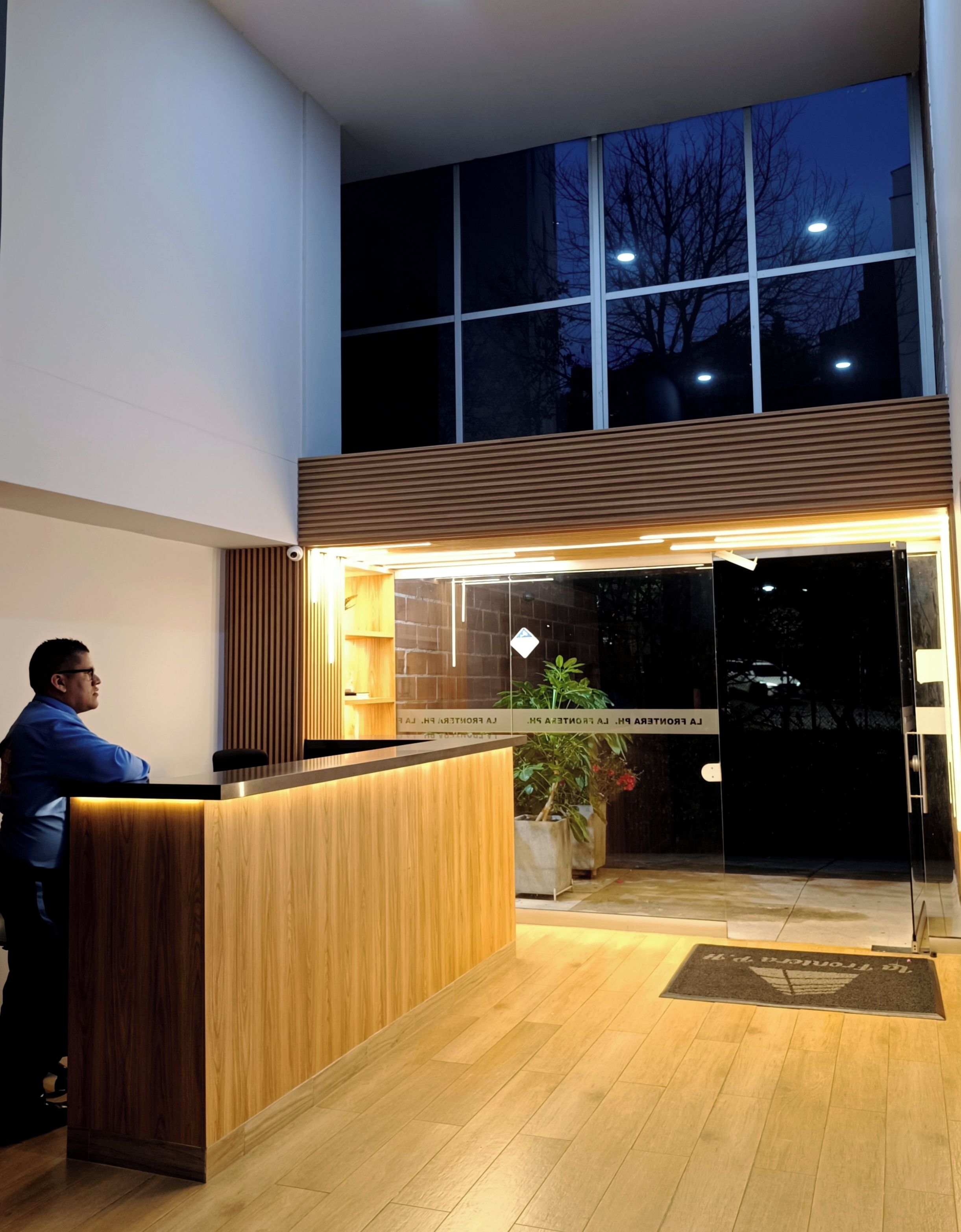 Un comptoir d’accueil avec un revêtement en bois, une plante en pot et une porte en verre donnant sur un espace intérieur.