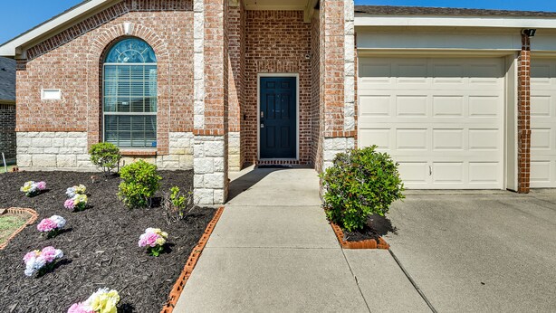 Une maison en briques avec un garage, une porte d’entrée et un petit jardin fleuri.