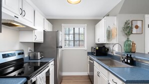 Eine moderne Küche mit weißen Schränken, einem Edelstahl-Kühlschrank, einer schwarzen Mikrowelle und einer blauen Arbeitsplatte.