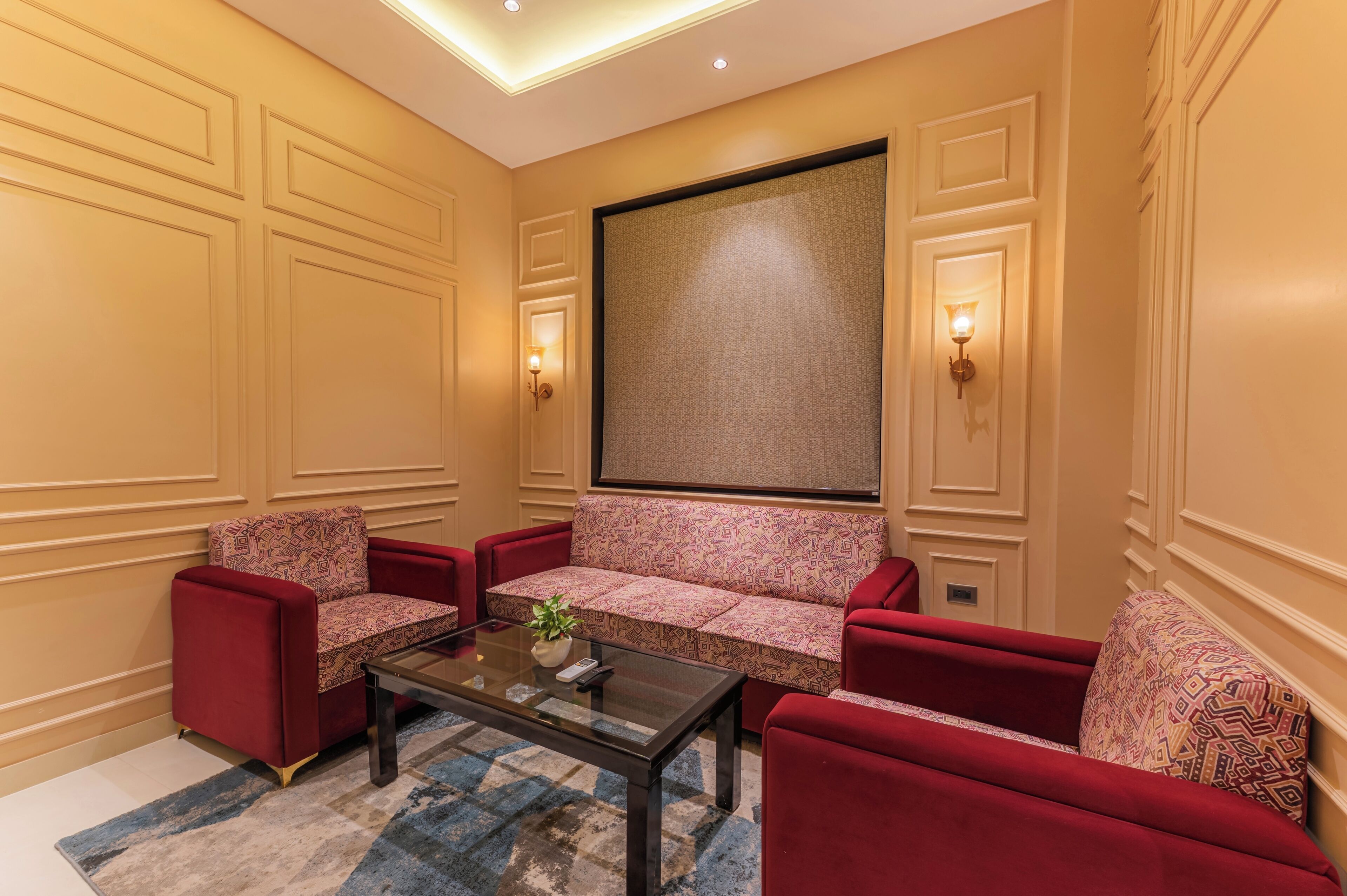 Una habitación con sofá, sillones, una mesa de centro y una pantalla grande.
