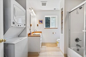 Ein kleines Badezimmer mit Waschmaschine, Spüle mit Holztischplatte, Toilette und Dusche.