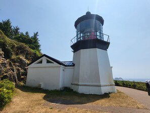 Ein Leuchtturm mit weiß-schwarzer Struktur, ein kleines Nebengebäude und ein befestigter Weg mit Grünflächen.