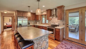 A spacious kitchen with a large island, wooden cabinets, and a stone accent wall. - Secluded & Spacious Cabin W/ a Spa and Garage (Sturgis)
