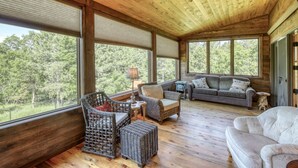 A spacious room with large windows, wicker furniture, and a grey sofa. - Secluded & Spacious Cabin W/ a Spa and Garage (Sturgis)