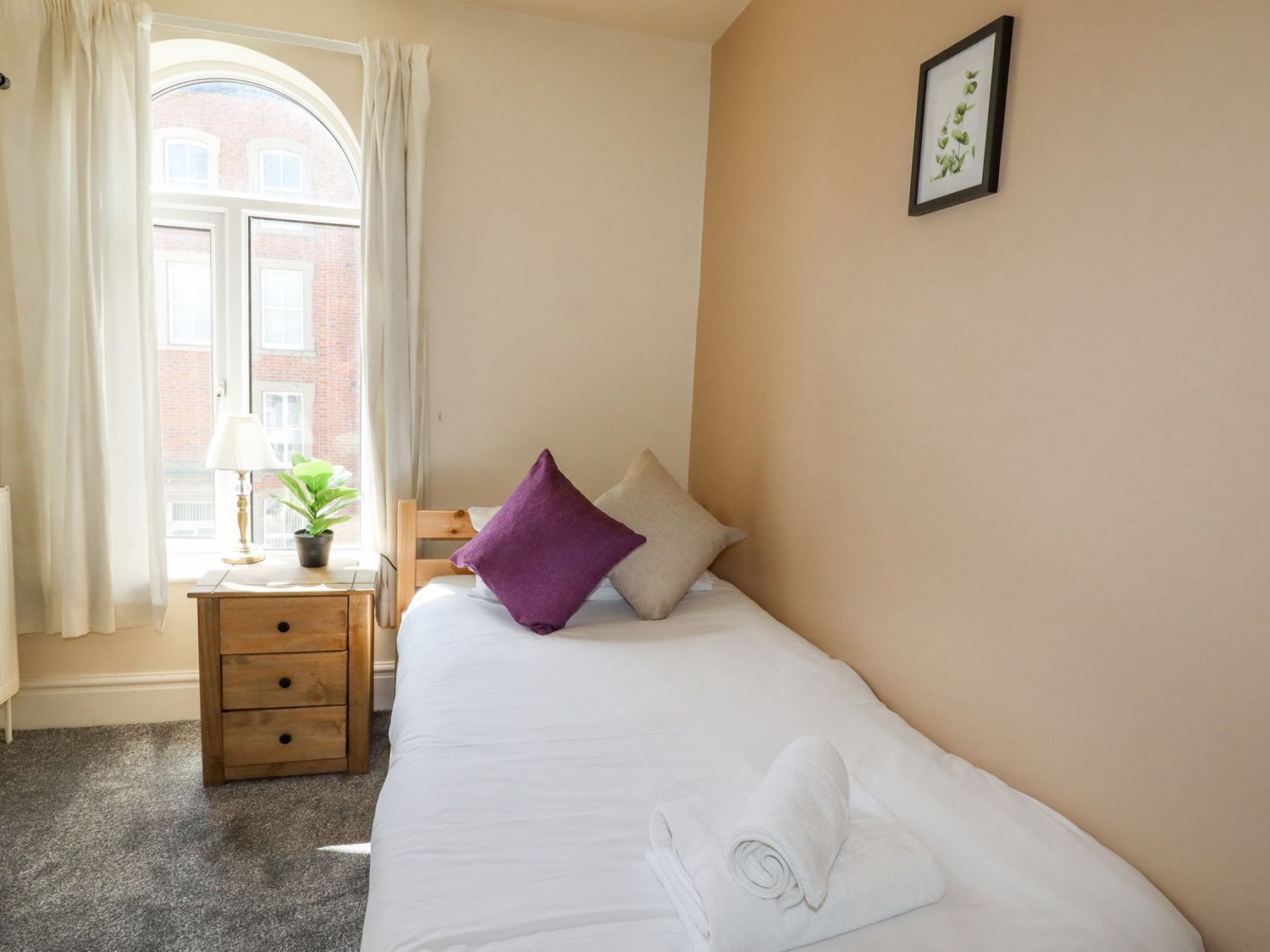 A hotel room with a bed, a nightstand, a lamp, a window with curtains, and a framed picture on the wall.