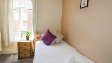 A hotel room with a bed, a nightstand, a lamp, a window with curtains, and a framed picture on the wall.
