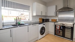 Una cocina moderna con armarios blancos, una campana extractora de acero inoxidable, un horno empotrado y una lavadora.