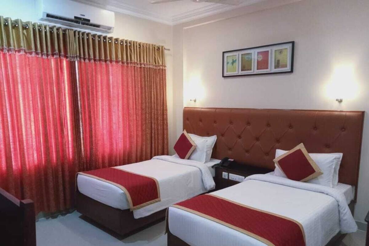 Ein Hotelzimmer mit zwei Betten, einem roten Vorhang, einem gerahmten Bild an der Wand und einer Klimaanlage.