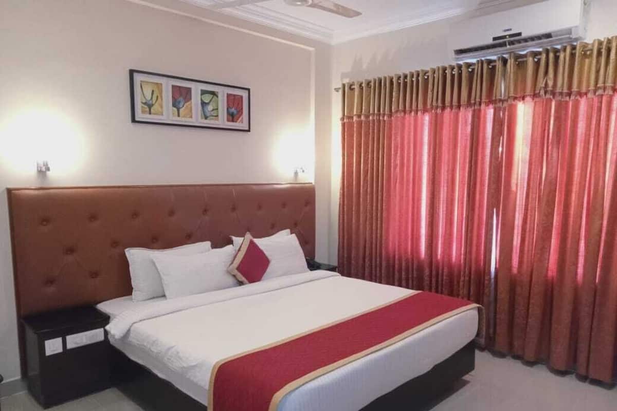 Ein Hotelzimmer mit einem großen Bett, einem Kopfteil, einem Nachttisch und einem Vorhangfenster.