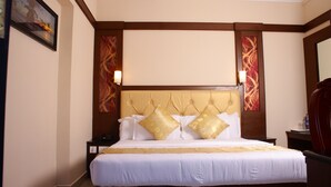 A hotel room with a large bed, wooden headboard, and two bedside tables. - Hotel Sahana Castle (Nagercoil)