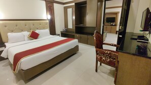 A hotel room with a large bed, a desk, a chair, a television, and a mirror. - Hotel Sahana Castle (Nagercoil)