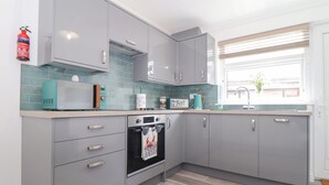 A modern kitchen with grey cabinets, a microwave, a kettle, and a fire extinguisher. - Apple Tree Bungalow (Redruth)