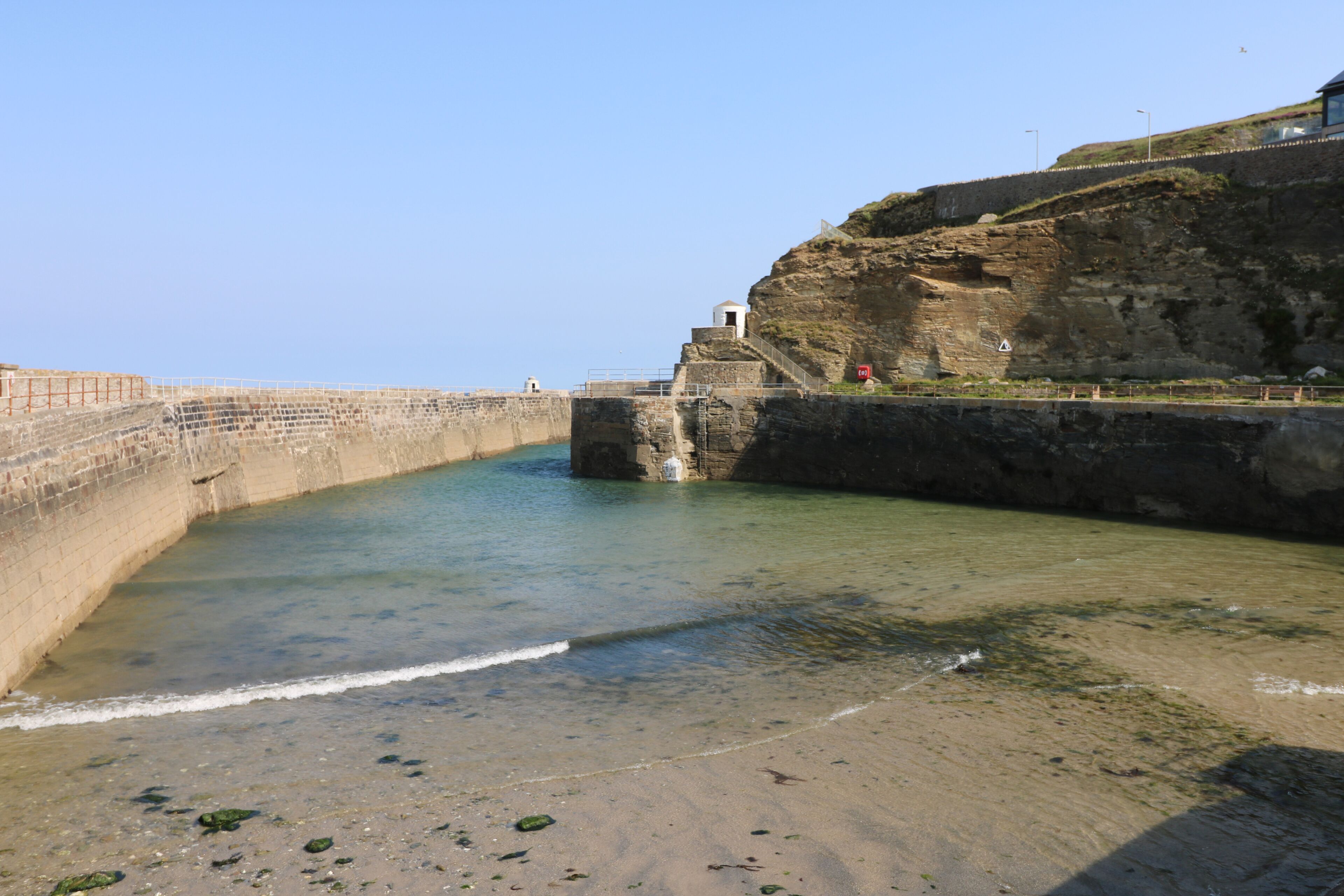 Un paysage côtier offrant une vue dégagée sur la mer, avec un mur de pierre et un petit bâtiment situé sur une falaise.