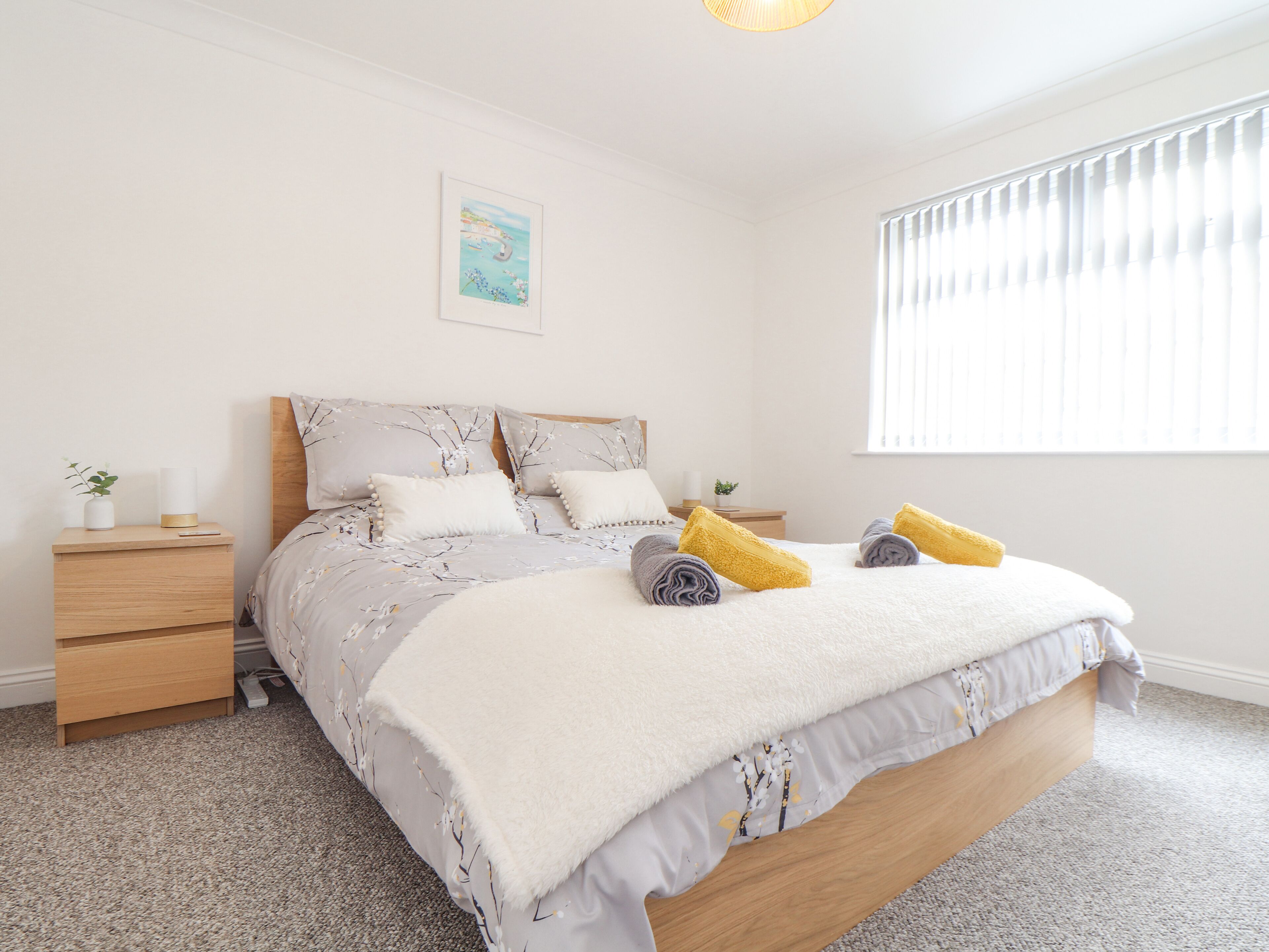 A bedroom with a bed, a nightstand, a bedside table, and a window with blinds.