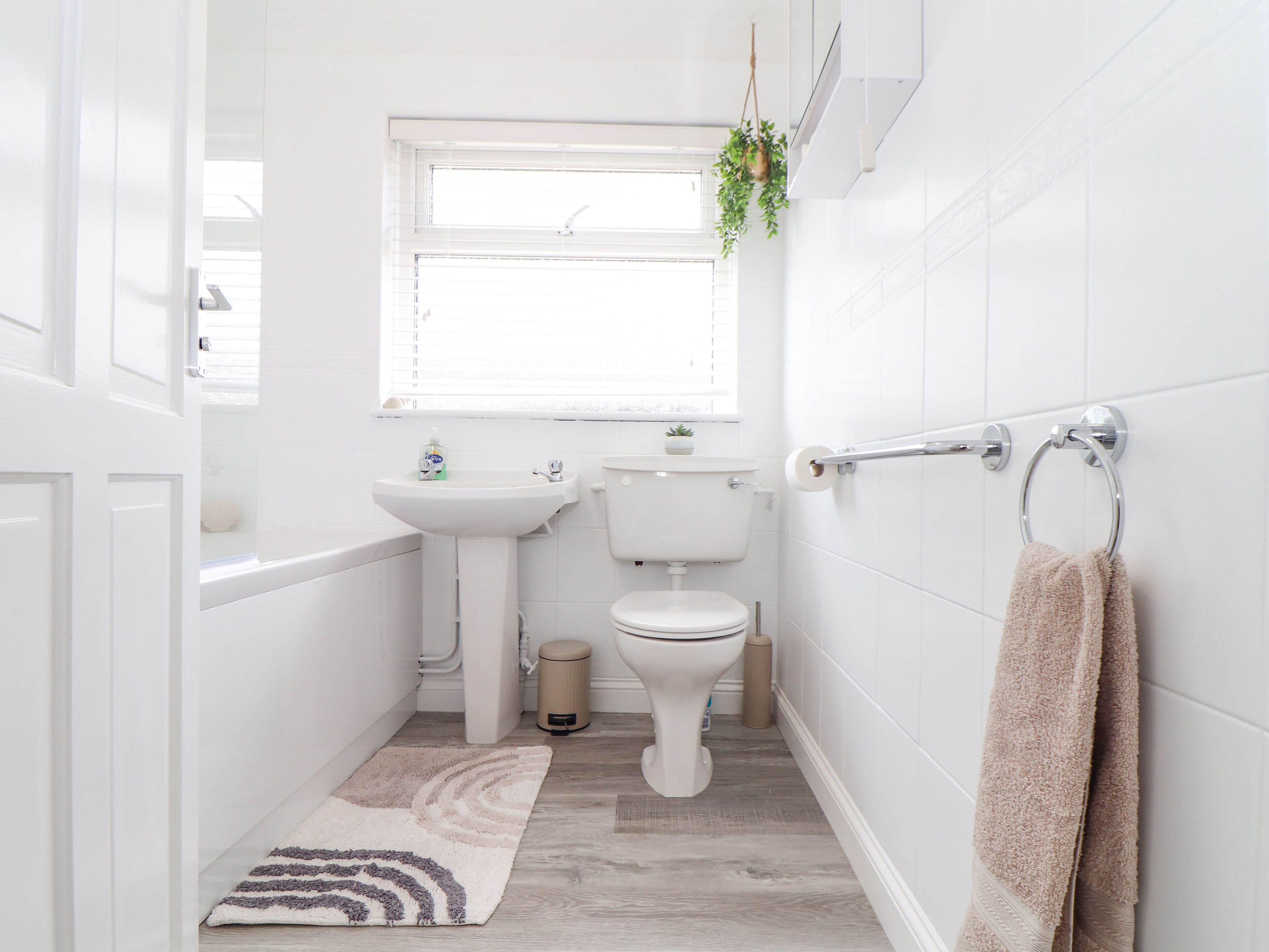 Un baño pequeño y moderno con sanitarios blancos, una ventana, un lavabo, un inodoro y un perchero para toallas.