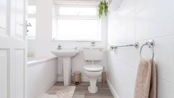 Un baño pequeño y moderno con sanitarios blancos, una ventana, un lavabo, un inodoro y un perchero para toallas.