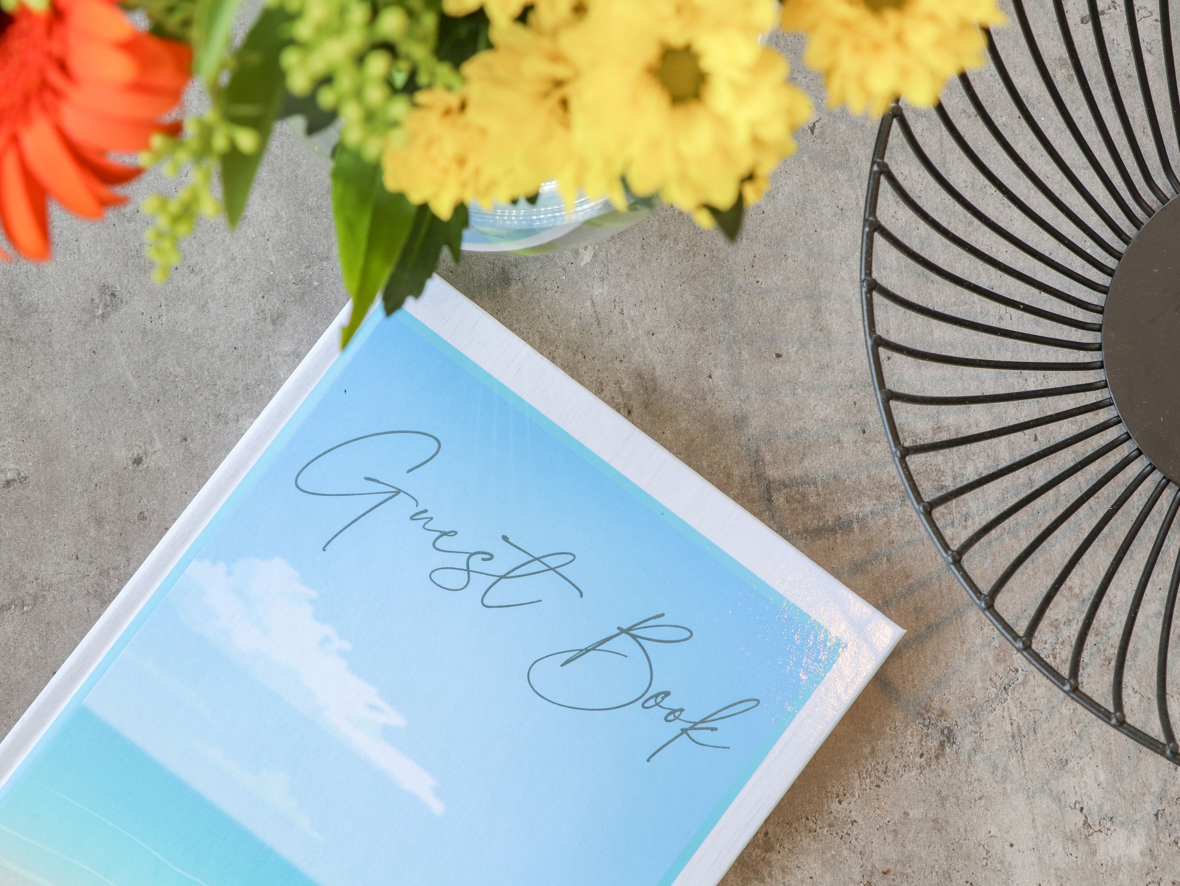 A guest book on a table with a metal decorative piece and flowers.