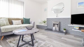 A modern living room with a grey sofa, a round coffee table, a fireplace, and a flat-screen TV. - Apple Tree Bungalow (Redruth)
