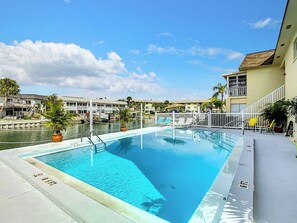 Une piscine rectangulaire dotée d’une terrasse blanche, entourée de chaises longues et de plantes en pot.
