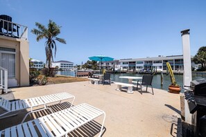 Eine Uferterrasse mit Liegestühlen, einem Tisch und Grillplatz.