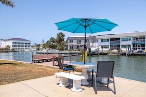 Une terrasse au bord de l’eau, avec une table et des chaises, un banc et un parasol bleu.