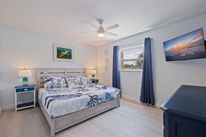 Ein Schlafzimmer mit einem Bett, einem Deckenventilator, einem Fenster mit Vorhängen, einem Fernseher und Kunstwerken an der Wand.