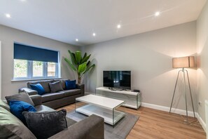 A modern living room with a sofa, coffee table, TV, and floor lamp. - Spacious 4BR Bungalow in Leicestershire (Bagworth)