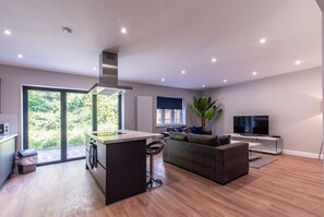 A modern kitchen with a central island, a dining area with a sofa, and a TV on a stand.