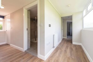 Experience the comfort of a well-appointed hallway with a glass-enclosed shower, radiator, and wooden floor.