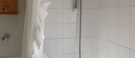 Una ducha con cabezal de ducha manual, cortina de ducha y pared con azulejos.