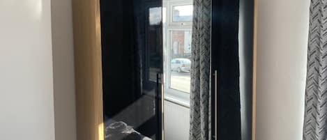 A room with a mirrored wardrobe, a window with curtains, and a view of the outside.