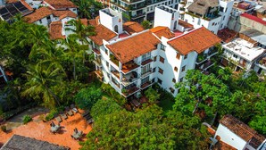 Un edificio a più piani con tetto in tegole rosse, circondato da vegetazione lussureggiante e palme.