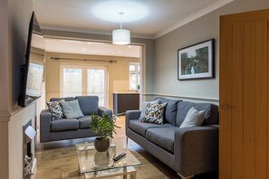 A living room with two grey sofas, a glass coffee table, a potted plant, a television, and a framed picture on the wall. - 5-BR Home w/ Garden, Near Cheltenham Race Course (Charlton Kings)