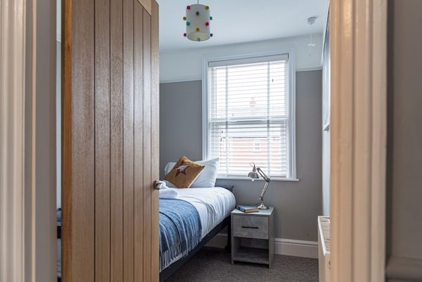 Un dormitorio con cama, mesita de noche, lámpara y ventana con persianas.